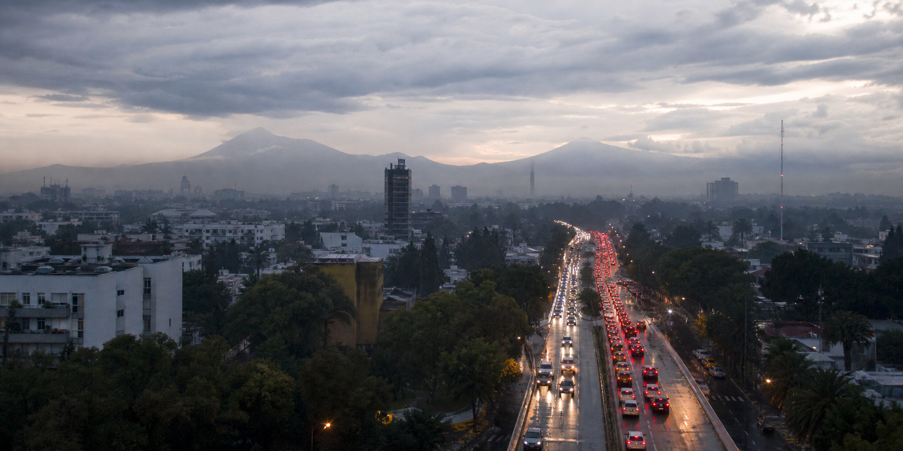 Tráfico vehicular en una avenida de la Ciudad de México al amanecer, con pavimento mojado y cielo nublado.