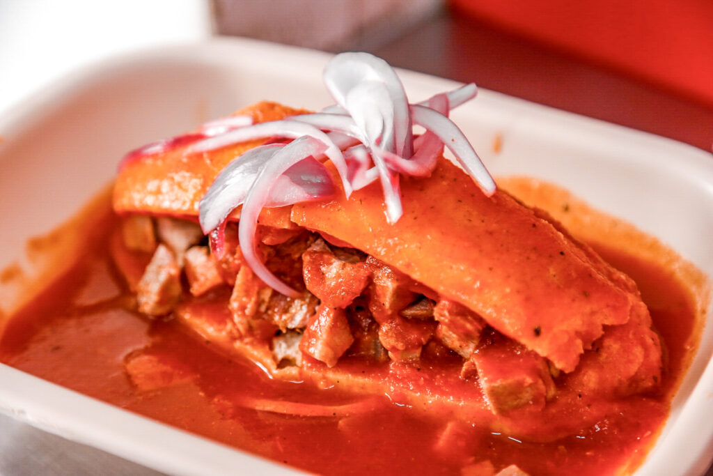 Torta ahogada de Guadalajara servida con salsa de jitomate, carnitas, cebolla encurtida y limón.